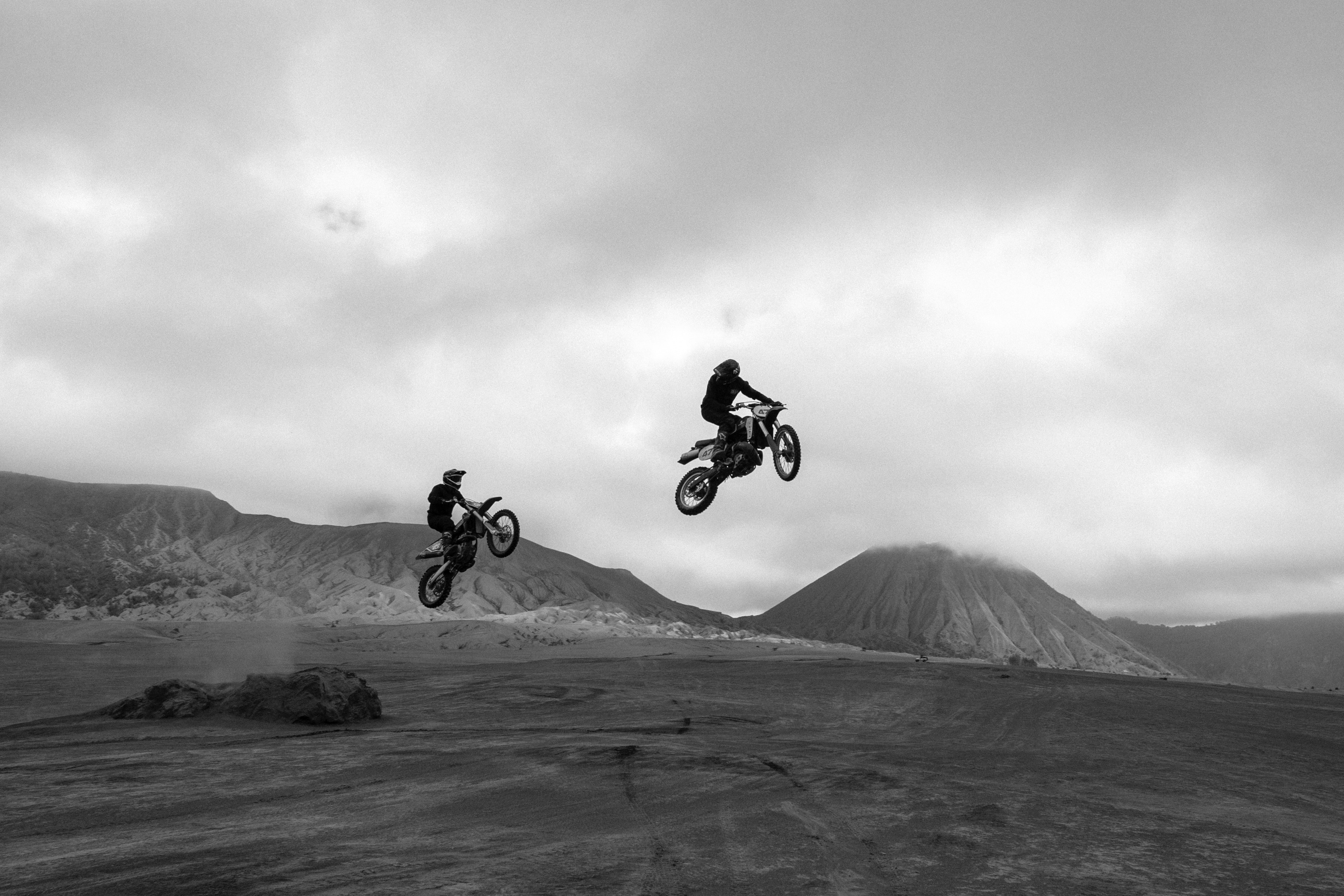 Two dirt bike riders take a jump in an old gravel pit, soaring through the air.