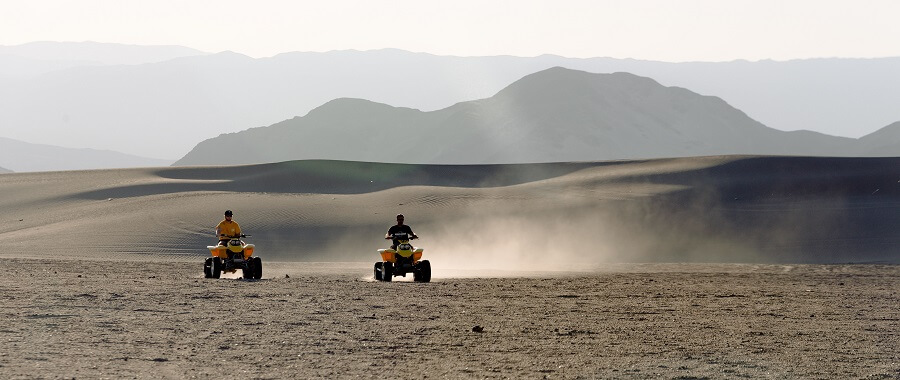 Two people riding ATVs through the desert