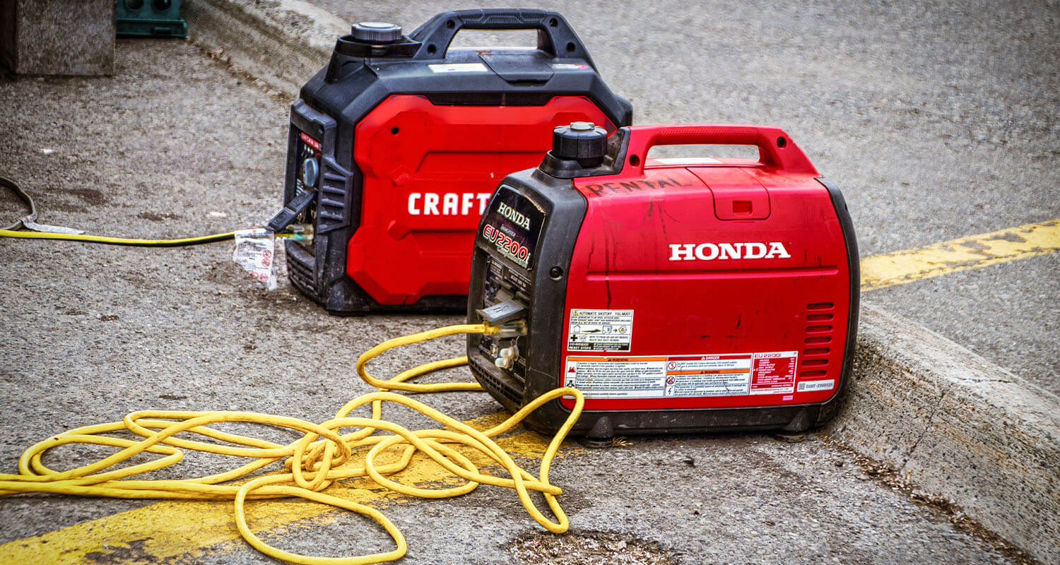 Red and Black Honda and Craftsman portable generators sitting in parking lot with cords leading to whatever is being charged.
